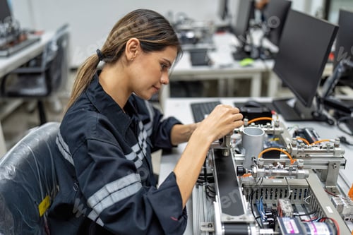 Preview: Girl engineer sitting in robot fabrication room quality checking electronic control board
