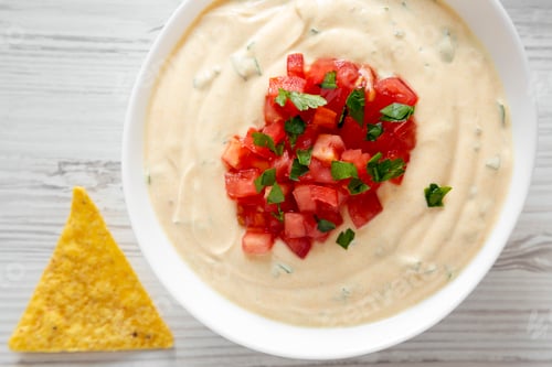 Preview: Homemade cheesy dip in a bowl, yellow tortilla chips, top view. From above, overhead, flat lay.