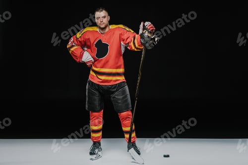 Preview: full length view of professional ice hockey player standing with hand on waist and looking at camera
