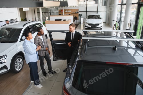 Preview: Car salesman showing new car to african american couple in dealership