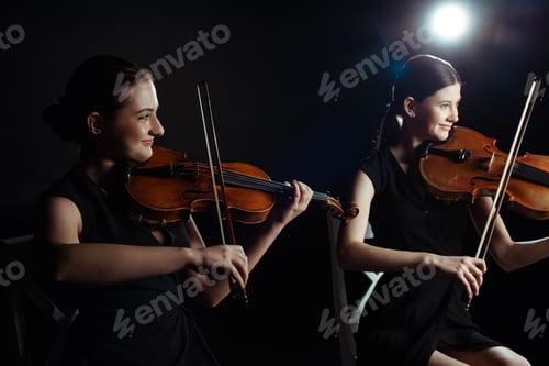 Preview: happy attractive musicians playing on violins on dark stage with back light