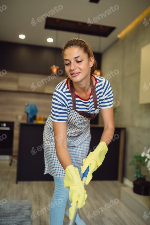 Preview: Young brunette wearing apron and rubber gloves while mopping floors at home