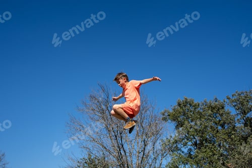 Preview: Young boy jumping high in the air with blue sky background