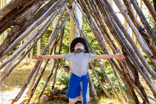 Preview: Young boy looking up, standing in a tunnel made of tree logs.