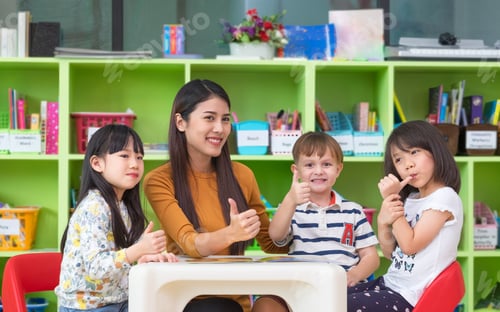 Preview: Asian female teacher and mixed race kids thumbs up in classroom