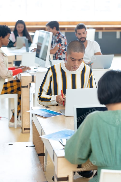 Preview: Young Mixed-race Businessman working on desk while colleagues working around him