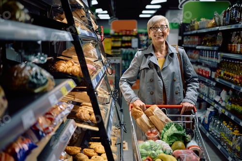 Preview: Happy senior woman with shopping cart at the store looking at camera.
