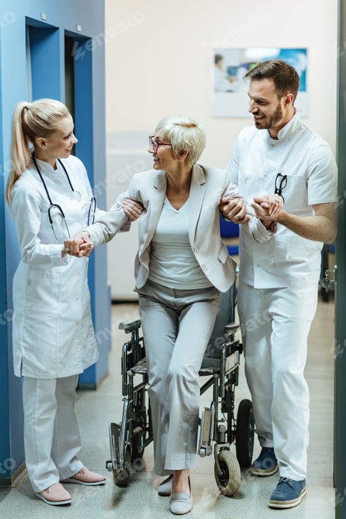 Preview: Happy doctors helping mature woman to get up from a wheelchair at clinic.