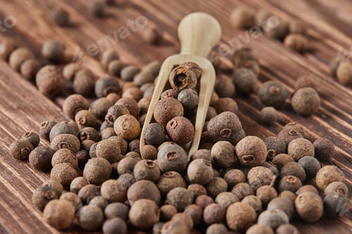 Preview: Large black peppercorns with wooden spatula are scattered over wooden vintage background
