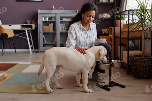 Preview: Cute dog eating food at home with caring young woman watching