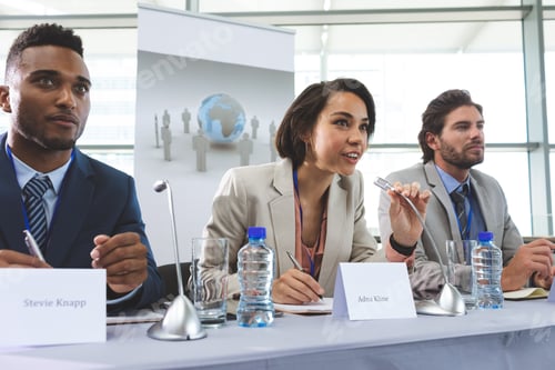 Preview: Front view of young mixed race business people sitting at table in seminar