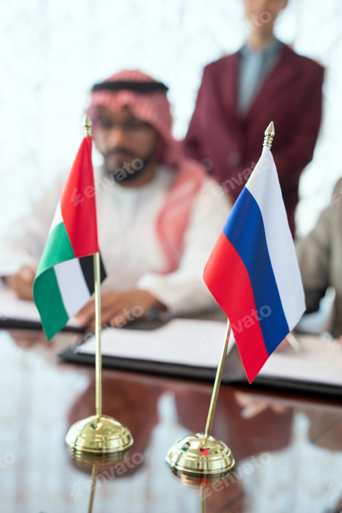 Preview: Flags of Russian Federation and United Arab Emirates on table against delegates