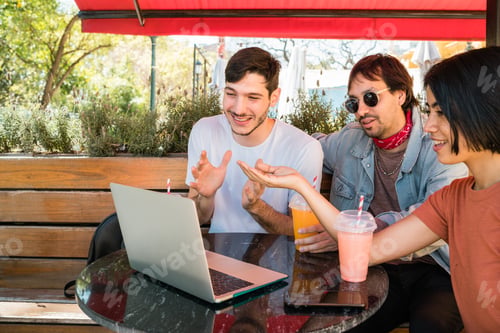 Preview: Three young friends using laptop at coffee shop.