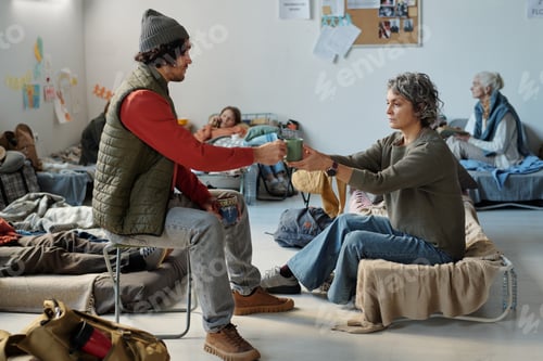 Preview: Man passing cup of tea to female refugee