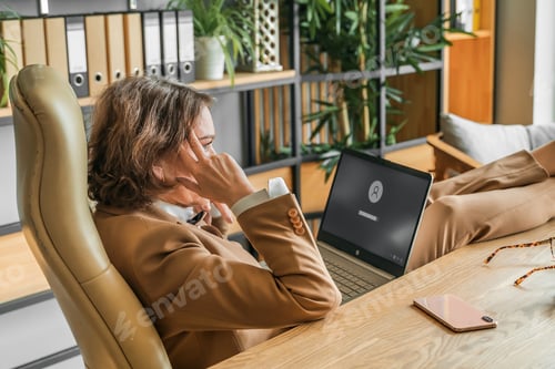 Preview: Confident stylish mature middle aged elderly woman in office. Workplace with laptop, using talking b