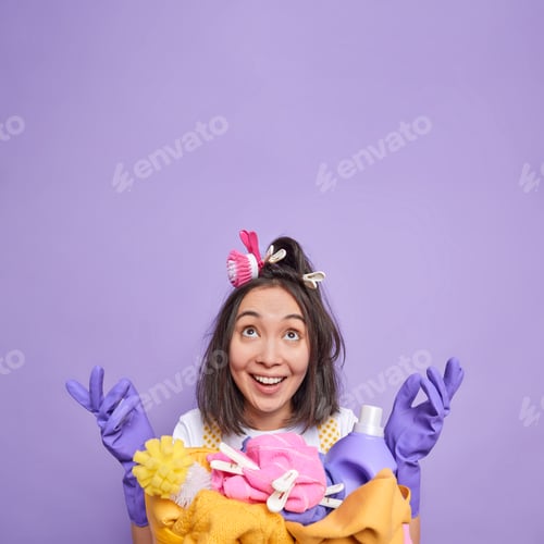 Preview: Vertical shot of happy Asian housewife spreads palms and focused overhead smiles gladfully stands