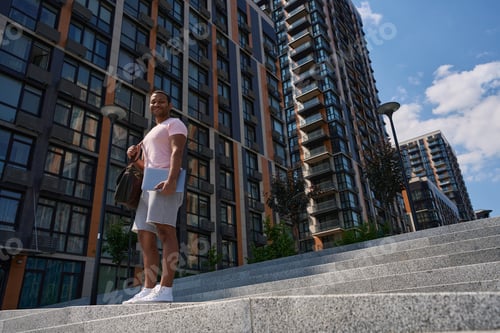 Preview: Joyful guy with laptop posing for camera in business district