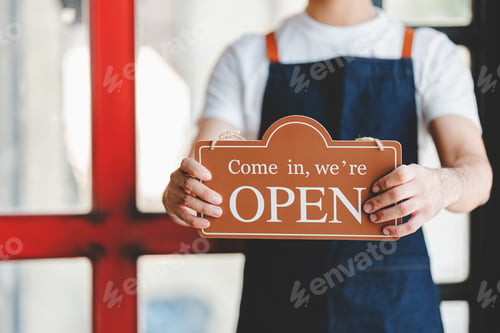 Preview: The store owner holds a sign in front of the store ready to serve.