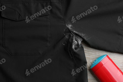 Preview: Black shirt with stain and deodorant on wooden background, closeup