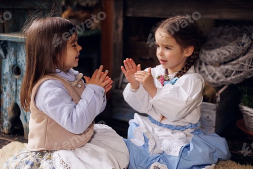 Preview: Two little sisters girls playing game Ladushki. Retro style clothes