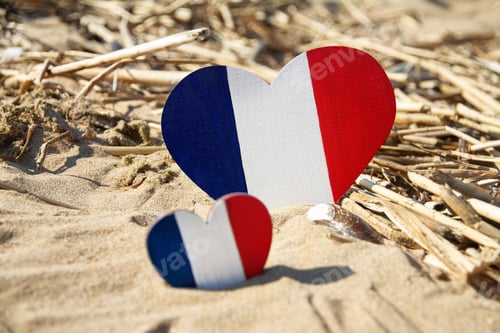 Preview: two wooden hearts painted in colors of flag of France blue white red lies on sand of beach