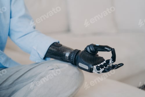 Preview: Cyber hand of disabled person which is sitting in lotus pose on couch. Robotic arm in meditation.