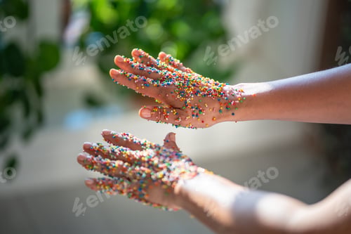Preview: Sticky female hands in colorful sprinkles for cupcakes, donuts, cakes in sunlight. Dessert topping