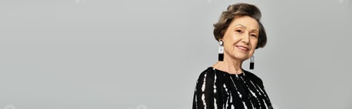 Preview: A stylish woman in her 60s poses gracefully, showcasing trendy attire against a grey backdrop