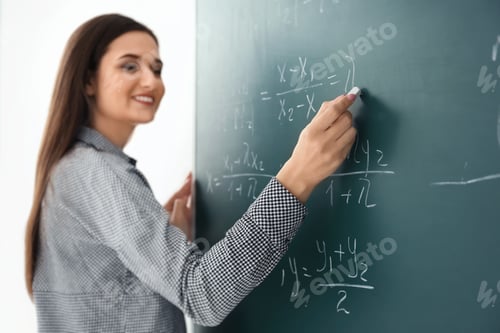 Preview: Young female teacher writing on blackboard in classroom