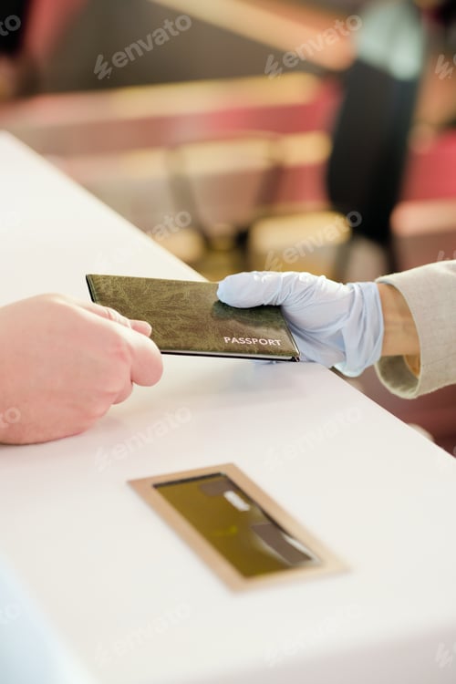 Preview: Gloved hand of female receptionist standing by counter and giving back passport of male passenger