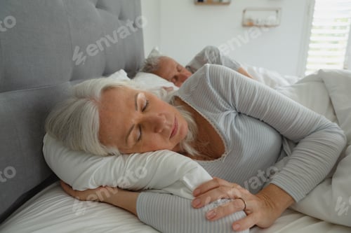 Preview: Front view of active senior Caucasian couple sleeping together in bed in bedroom at home