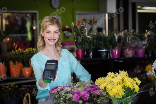 Preview: Female florist standing behind flower shop counter, presenting card terminal near bouquets
