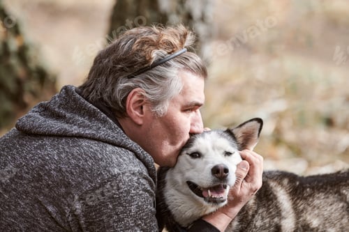 Preview: Adult man in gray sweatshirt hugs and kisses Siberian Husky dog, true love of human and pet