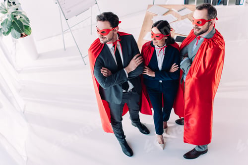 Preview: high angle view of super businesspeople in masks and capes with crossed arms in office