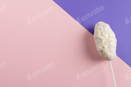 Preview: Horizontal image of homemade white candy floss on stick, on pink and purple with copy space