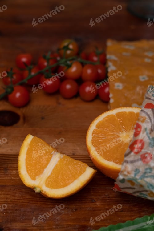 Preview: Sliced orange and tomatoes pouring out of beeswax wrap on a rustic table