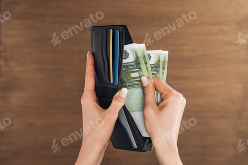 Preview: top view of woman puting euros banknotes in wallet on wooden background