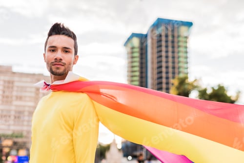 Preview: Young latin homosexual man with gay pride parade rainbow flag. Lifestyle superhero cape