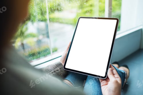Preview: a woman holding and using digital tablet with blank white desktop screen while sitting