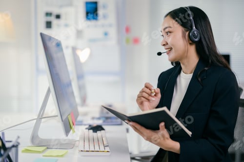Preview: Efficient asian businesswoman multitasks at her desk, handling customer service calls with professio