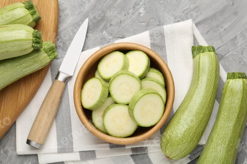 Preview: Fresh ripe zucchinis with knife on grey textured table, flat lay. Whole and cut