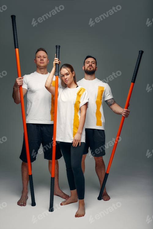 Preview: Two men and woman aikido fighters with wooden fight stick posing in studio, fight demonstration
