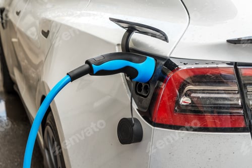 Preview: White electric car being charged at a charging station. Green energy concept.