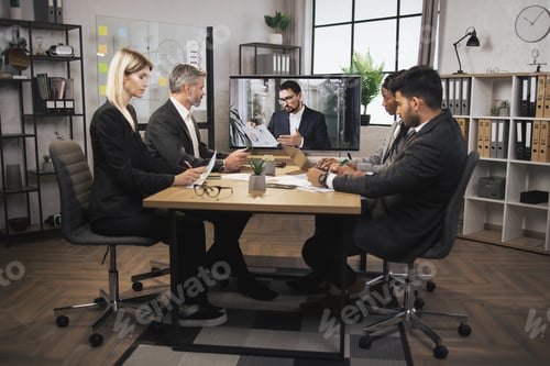 Preview: Team of four focused multiethnical businesspeople looking at screen, having video conference