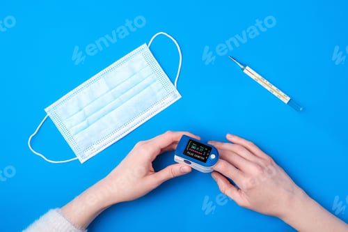 Preview: Person using pulse oximeter device on finger near to thermometer and medical mask