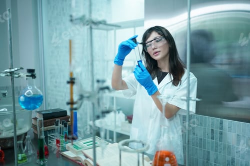 Preview: Young scientist in white lab coat working with binocular microscope in the material science lab