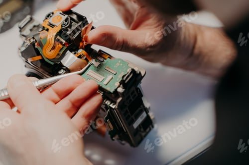 Preview: Hands of handyman repairing broken digital camera, holds special tweezers, works in workshop