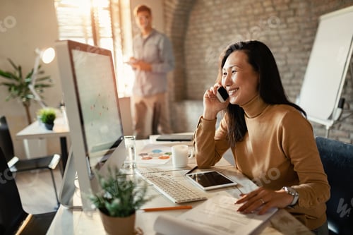 Preview: Happy Asian freelance worker communicating on cell phone in the office.
