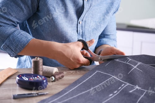 Preview: Tailor cutting fabric at table in atelier, closeup