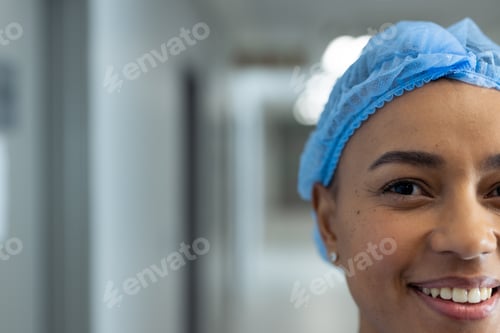 Preview: Portrait of half face of smiling biracial female healthcare worker in hospital corridor, copy space